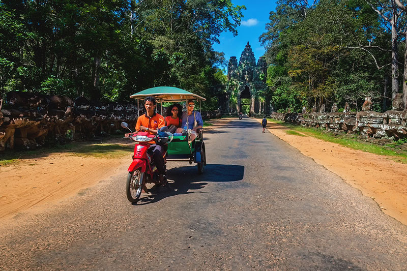 Tuk-tuk Mas se a cidade peca em não oferecer formas de transporte convencionais, a oferta de tuk-tuks é enorme. Eles estão espalhados por todos os cantos da cidade, nas praças, portas de hotéis, mercados… em qualquer lugar você vai achar um deles. Andar de tuk-uk em Siem Reap é muito barato, uma corrida de uns 8 quilômetros custa 2 dólares e a concorrência é tão grande que os caras te esperam na porta para poder garantir uma corrida de volta para o hotel. Apesar do calorão que faz em Siem Reap, é uma viagem agradável, muitas vezes rola uma poeira na cara mas faz parte da aventura. Você pode contar com eles para te levar da cidade até os templos de Angkor Wat e ainda circular o dia todo com eles pelo complexo de templos, que é enorme. Taxi Eles são raridade, mas existem. Não usam nenhuma sinalização que indique que se trata de um taxi e muito menos usam taxímetro. No fundo são carros particulares que prestam esse serviço. A maioria atendem os grandes hotéis e o preço é combinado antes das corridas. O difícil é encontrar um deles, na dúvida, conte com os tuk-tuks. Alugando uma moto Outra maneira muito usada para se locomover em Siem Reap é alugando uma moto, dessas do tipo lambreta, que são muito comuns nesse canto da Ásia. Você pode alugar os veículos em pequenas agências, mas alguns hotéis oferecem esse serviço para os clientes Bicicleta Para circular pela cidade você também pode alugar uma bike, o duro é pedalar naquele calorão. As ruas de Siem Reap são planas, o que facilita bastante a locomoção. A maioria dos hostels oferecem as magrelas para alugar e alguns fazem parte de um programa chamado The White Bicycles, que é uma cooperativa que aluga as bikes para turistas e a renda vai para famílias de vítimas de minas terrestres e instituições de caridade. O The White Bicycles é um projeto bem legal que existe em Siem Reap e vale muito a pena apoiar. As bikes são alugadas por 2 dólares a diária. Carro particular Essa é a maneira mais cômoda para ir de Siem Reap até o complexo de templos de Angkor e visitar todos os templos. Tuk tuk – transporte popular em Siem Reap